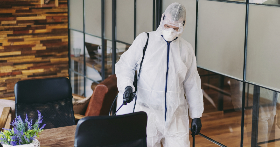 Man in protective suit and face mask spraying for disinfection in the office