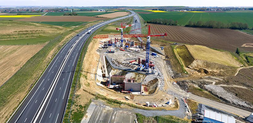 Vue aérienne du chantier au printemps 2026 : les deux culées prennent forme de part et d’autre de la future tranchée du Canal Seine-Nord Europe, tandis que l’A2 reste ouverte à la circulation sur son tracé provisoire.