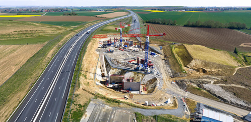 Vue aérienne du chantier au printemps 2026 : les deux culées prennent forme de part et d’autre de la future tranchée du Canal Seine-Nord Europe, tandis que l’A2 reste ouverte à la circulation sur son tracé provisoire.